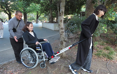 戸山公園内の樹木のある非舗装箇所をJINRIKIで車いすをけん引する様子